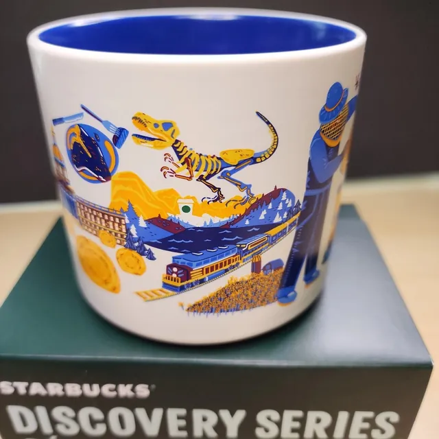 Starbucks Discovery Series Alberta mug with purple flowers, a blue bison, beehive boxes and a stepped waterfall around the word ALBERTA — side view