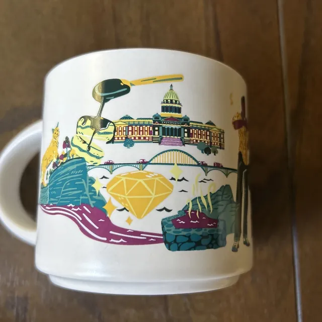 Starbucks Discovery Series Arkansas mug with a waterfall, bird, yellow flowers, pie and pickles around the word ARKANSAS — back view