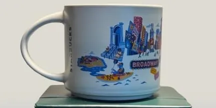 Starbucks Discovery Series Manhattan mug with a sandwich, a food cart, a saxophone, a dinosaur skeleton and a skyscraper around the word MANHATTAN — back view