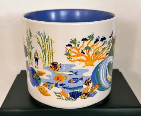 Starbucks Discovery Series Maui mug with a surfer on a wave, a pineapple, a seal and a waterfall around the word MAUI — side view