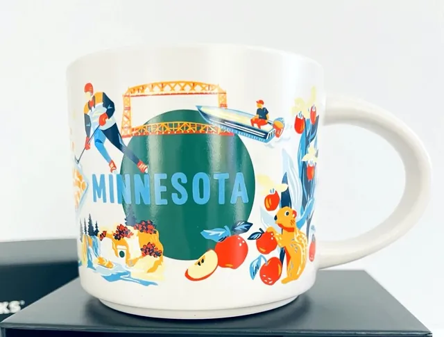 Starbucks Discovery Series Minnesota mug with a lift bridge, hockey player, apples and a skier around the word MINNESOTA