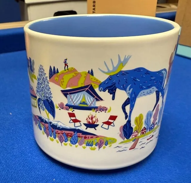 Starbucks Discovery Series New Hampshire mug with a red canoe, maple syrup bottle and ski poles around the words NEW HAMPSHIRE — side view