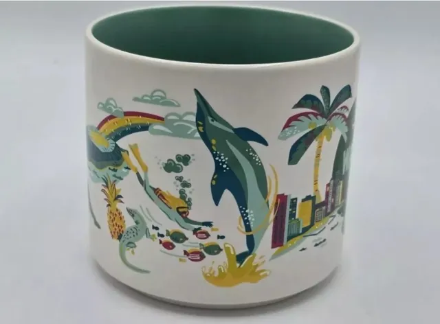 Starbucks Discovery Series Waikiki mug with a palm tree, an outrigger canoe, a yellow hibiscus and a surfboard around the word WAIKIKI — side view