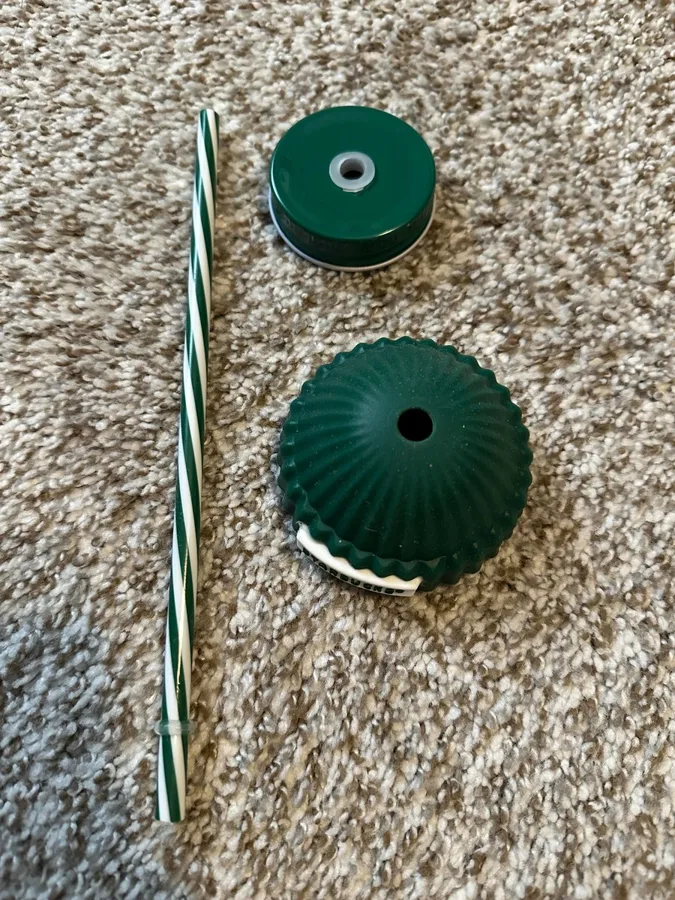 Straw, a green cap and the lid parts laid out on a carpet.