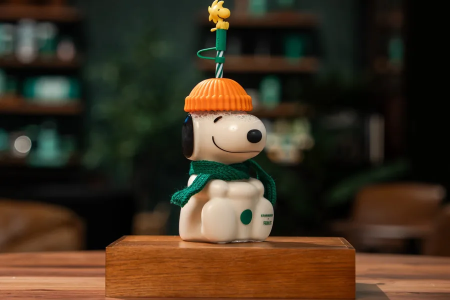 The Peanuts + Starbucks Snoopy glass cold cup with an orange beanie, green scarf and Woodstock straw topper