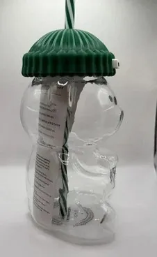 Starbucks Bearista original glass cold cup, a bear-shaped glass cup with a green ribbed beanie lid and a striped straw, side view
