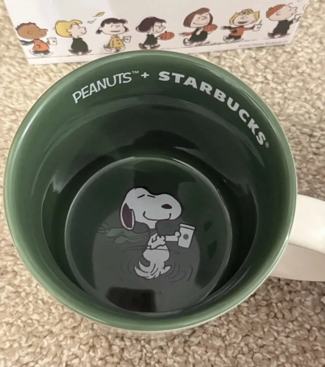 Starbucks Peanuts 14 oz ceramic mug showing the Peanuts gang with coffee cups and Snoopy asleep on a red doghouse, in its gift box, side view