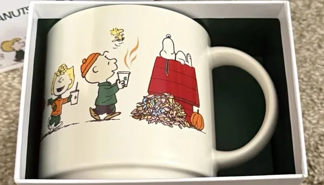 Starbucks Peanuts 14 oz ceramic mug showing the Peanuts gang with coffee cups and Snoopy asleep on a red doghouse, in its gift box