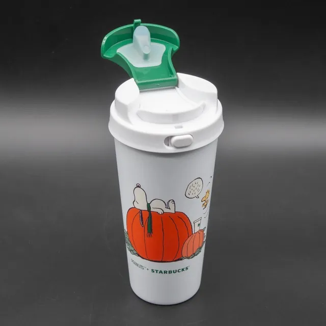 Starbucks Peanuts Great Pumpkin tumbler, white with Snoopy asleep on a pumpkin, next to its gift box, side view