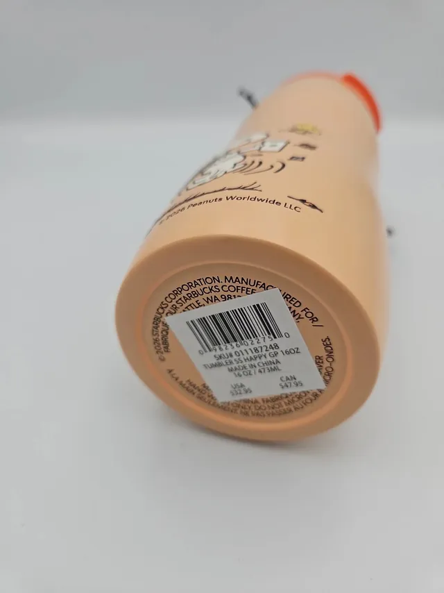 Starbucks Peanuts orange stainless steel tumbler with dancing Snoopy, a PEANUTS + STARBUCKS tag and a Woodstock and pumpkin charm, side view