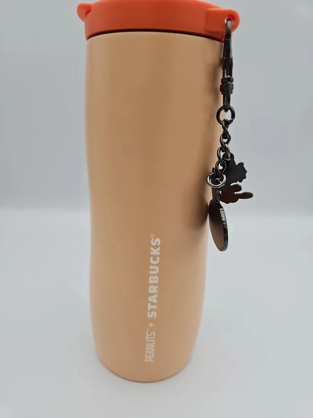 Starbucks Peanuts orange stainless steel tumbler with dancing Snoopy, a PEANUTS + STARBUCKS tag and a Woodstock and pumpkin charm, back view