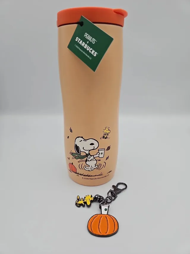 Starbucks Peanuts orange stainless steel tumbler with dancing Snoopy, a PEANUTS + STARBUCKS tag and a Woodstock and pumpkin charm
