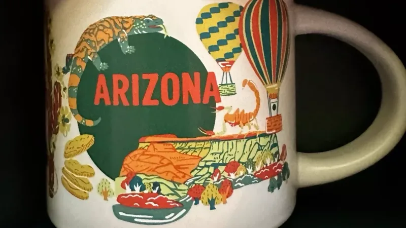 New Mexico Starbucks mug featuring adobe houses, a roadrunner, hot air balloons, a red chili pepper, and a "Welcome to Roswell" sign.