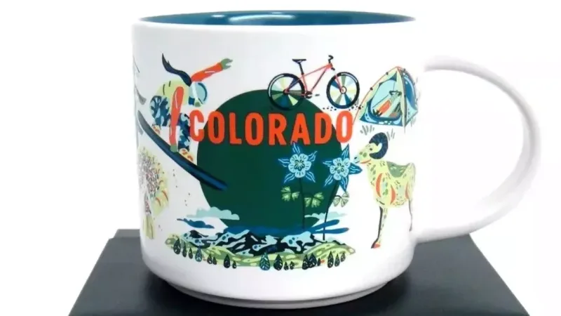 Starbucks Colorado Discovery Series mug with images of a skier, deer, butterfly, and mountains against a backdrop of outdoor adventure symbols.