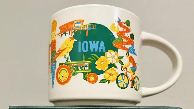 Illustration of the Iowa Discovery Series Starbucks mug showing a tractor, yellow bird, cyclist, flowers, and corn, symbolizing Iowa’s nature and agriculture.