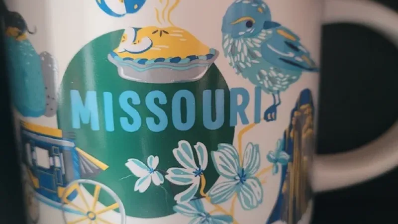 Missouri Discovery Series mug showing the Gateway Arch, stagecoach, dancing couple, riverboat, bee, and other iconic state symbols with vibrant colors