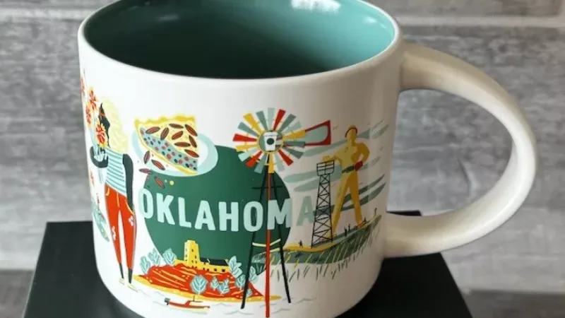 A Starbucks Discovery Series mug featuring illustrations of a woman holding flowers, Route 66 sign, buffalo, storm clouds, and a classic car, representing Oklahoma.