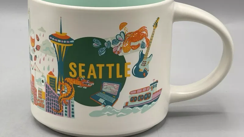 Seattle-themed Starbucks Discovery Series mug featuring illustrations of the Space Needle, kayakers, a Starbucks storefront, and other iconic city elements.