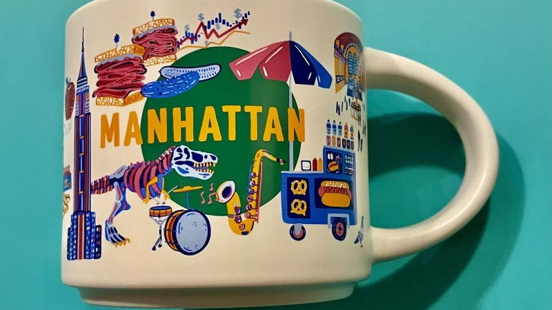 Manhattan Starbucks mug featuring the Empire State Building, Broadway, saxophone, and street food.