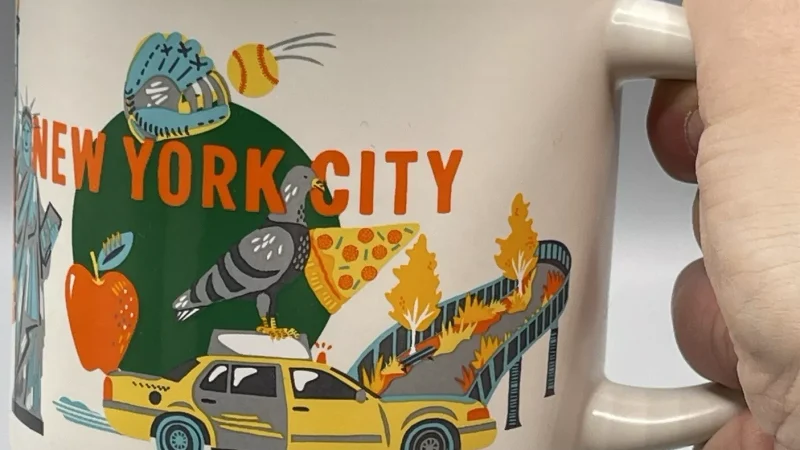 New York City Starbucks mug with illustrations of a yellow taxi, Statue of Liberty, pizza slice, and city skyline.