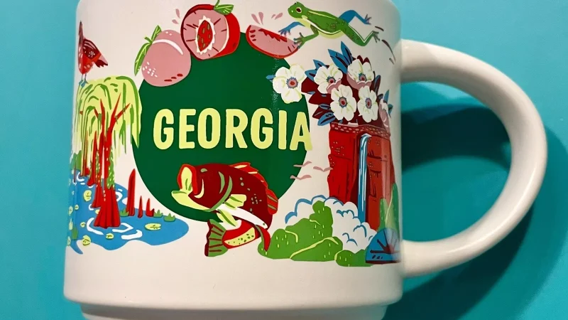 Georgia Starbucks mug with illustrations of peaches, bass fish, dogwood flowers, golfer, and cypress trees.