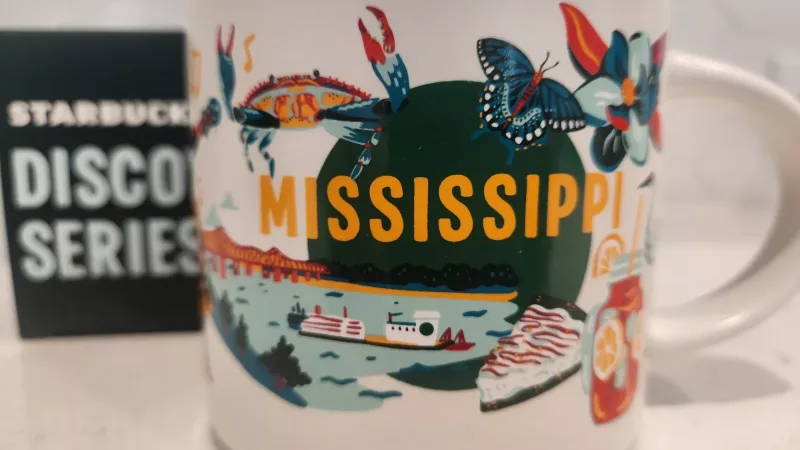 Starbucks Discovery Series mug featuring illustrations of Mississippi's natural beauty and cultural heritage, including crabs and butterflies.