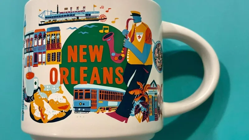 A Starbucks Discovery Series mug representing New Orleans, featuring a jazz musician, streetcar, and traditional Louisiana dishes, set against a colorful background.