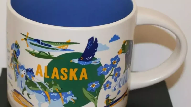 Alaska Starbucks mug showing a moose, snowy mountains, an igloo, a train, sled dogs, and a seaplane against a colorful background.